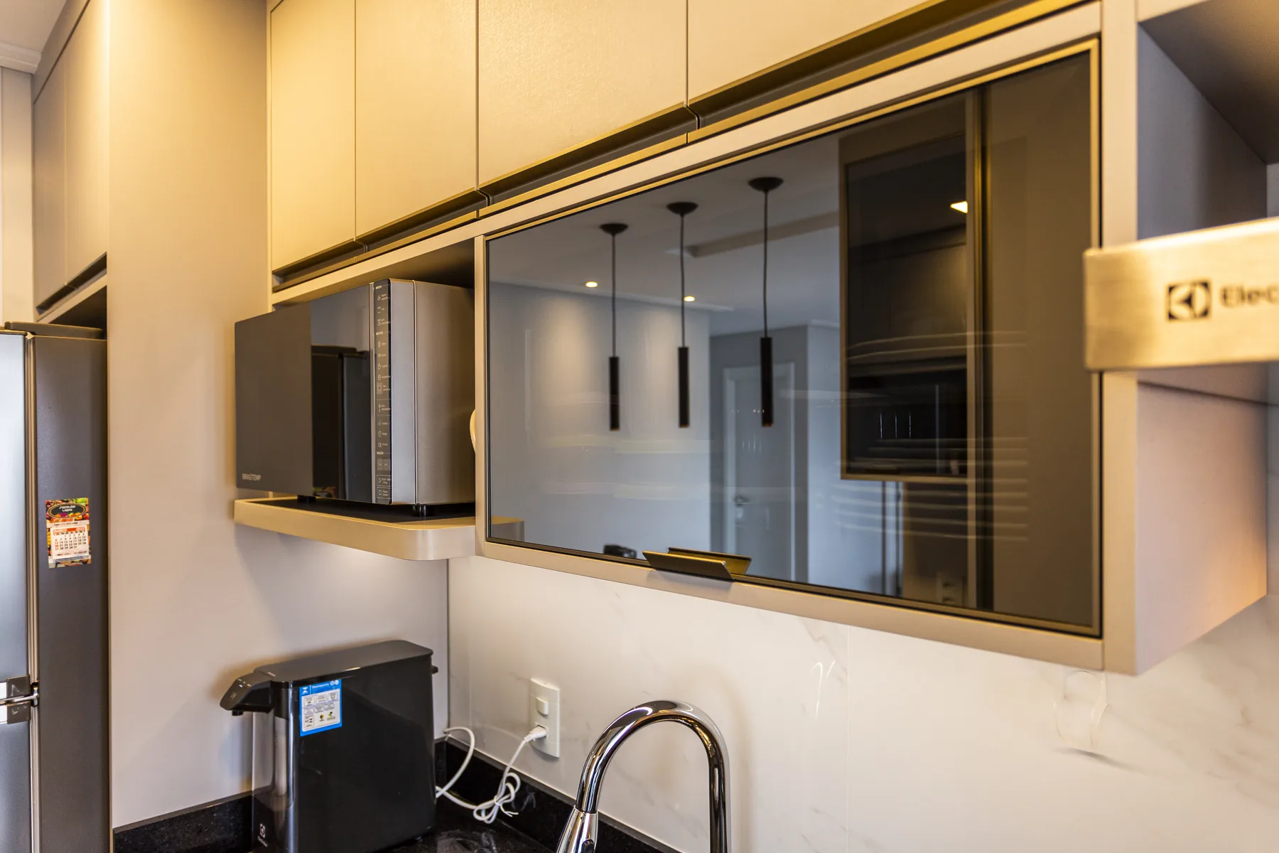 Detalhe de armário aéreo basculante com vidro fumê e perfil metálico em cozinha planejada, projeto Linear em Moema, São Paulo